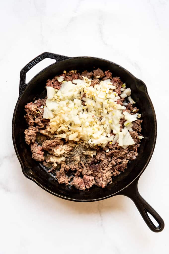 Adding chopped onions and garlic to browned ground beef in a large skillet.