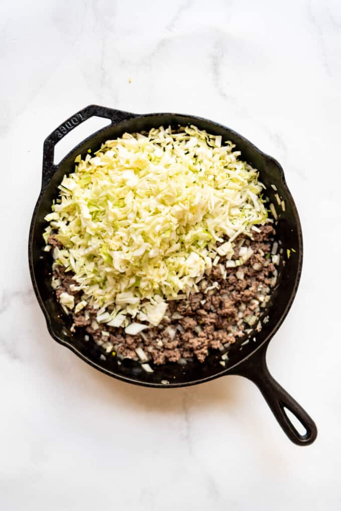 Adding chopped green cabbage to ground beef in a pan.