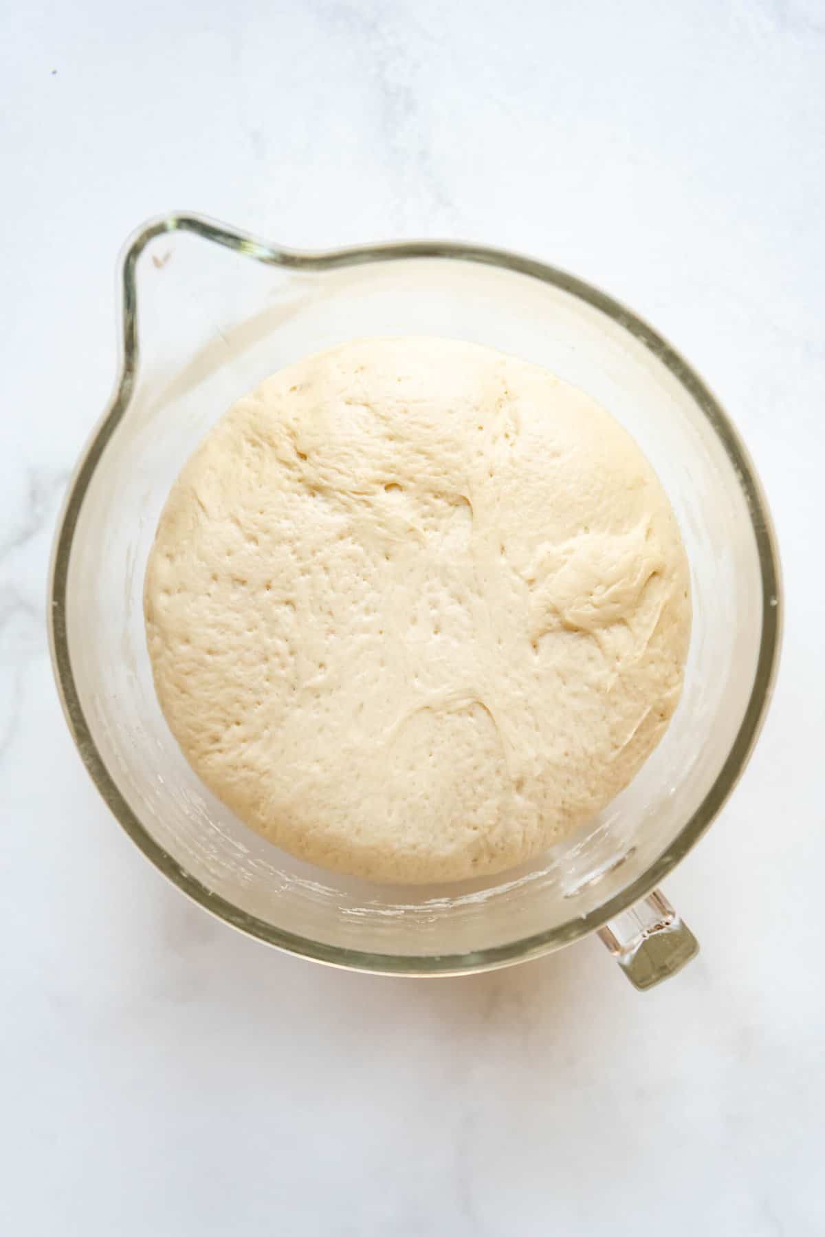 Risen Runza dough in a large glass mixing bowl.