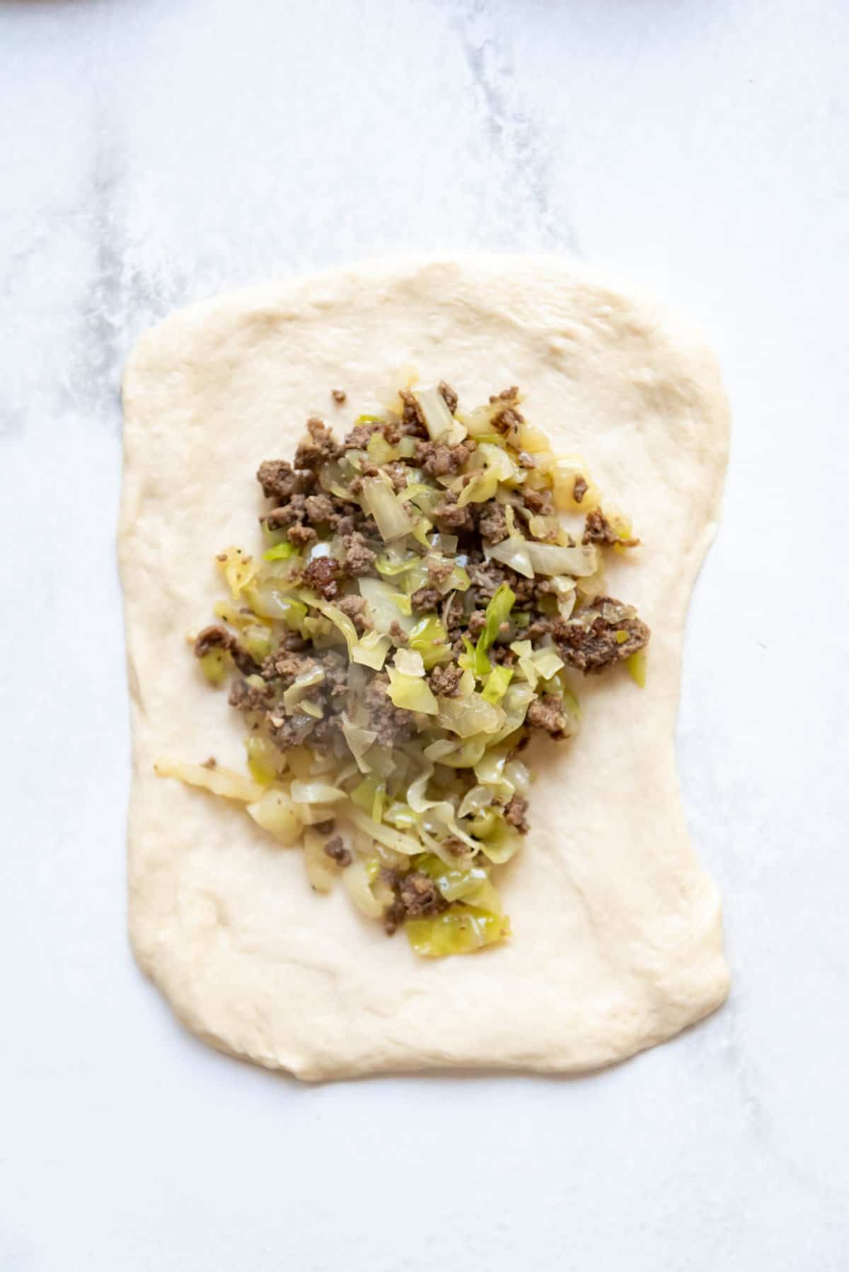 Adding ground beef and cabbage runza filling to a piece of bread dough.