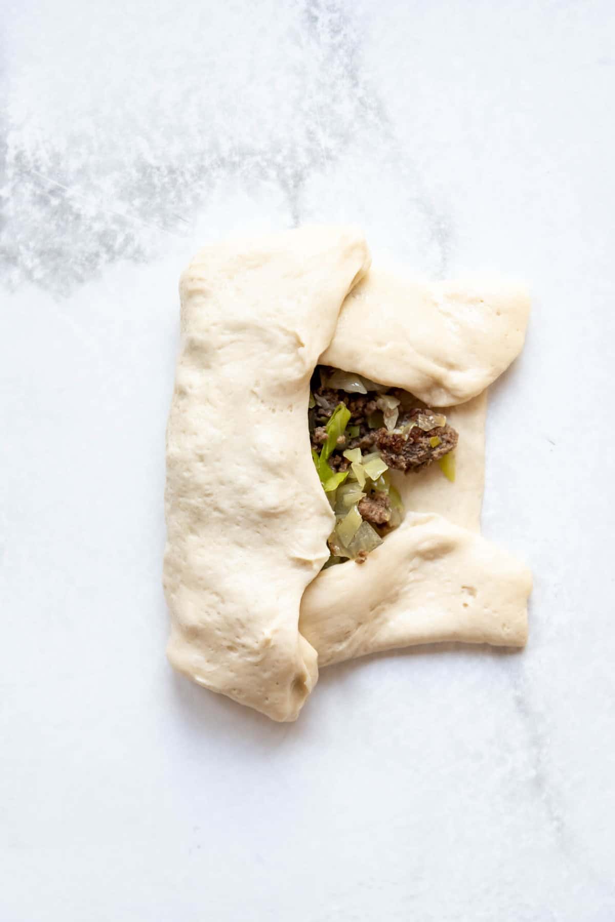 Folding an edge of dough over to enclose the filling for a homemade runza.