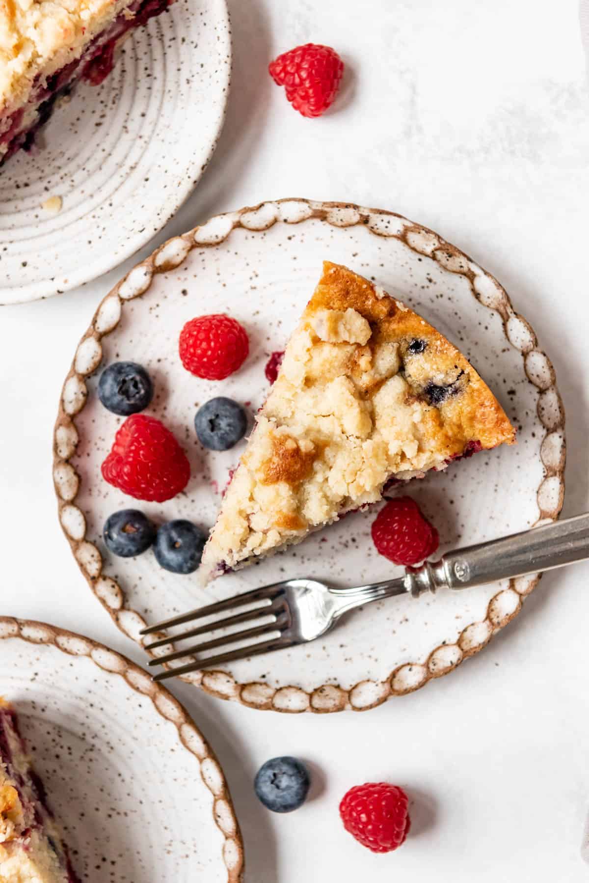 An overhead image of a slice of moist berry breakfast coffee cake on a plate with a fork.