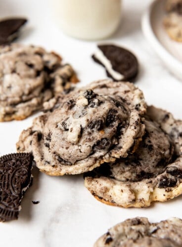 Oreo cheesecake cookies next to broken Oreo pieces and a glass of milk.