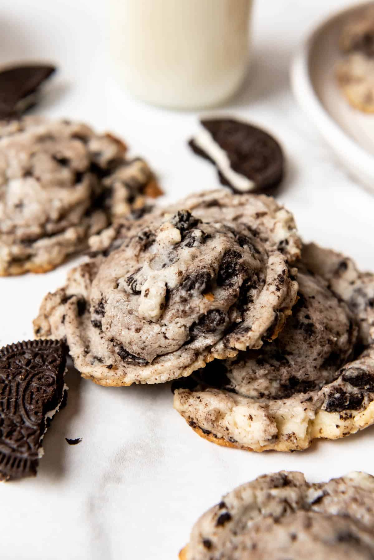 Oreo cheesecake cookies next to broken Oreo pieces and a glass of milk.
