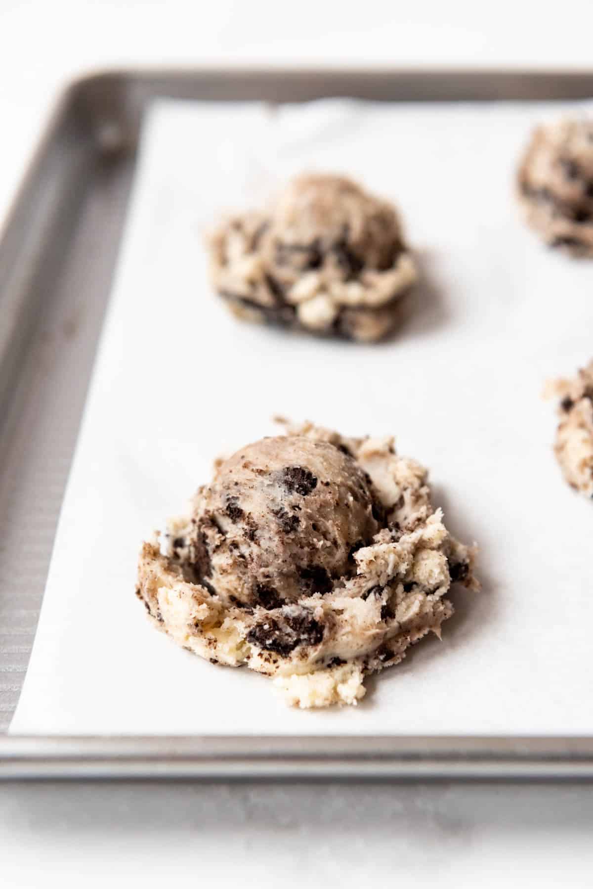 Oreo cheesecake cookie dough scooped onto a baking sheet lined with parchment paper.