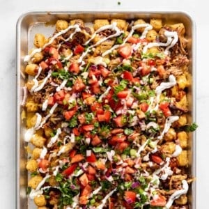A close image of loaded tater tot nachos (aka totchos) with pulled pork, pico de gallo, cheese, and sour cream.
