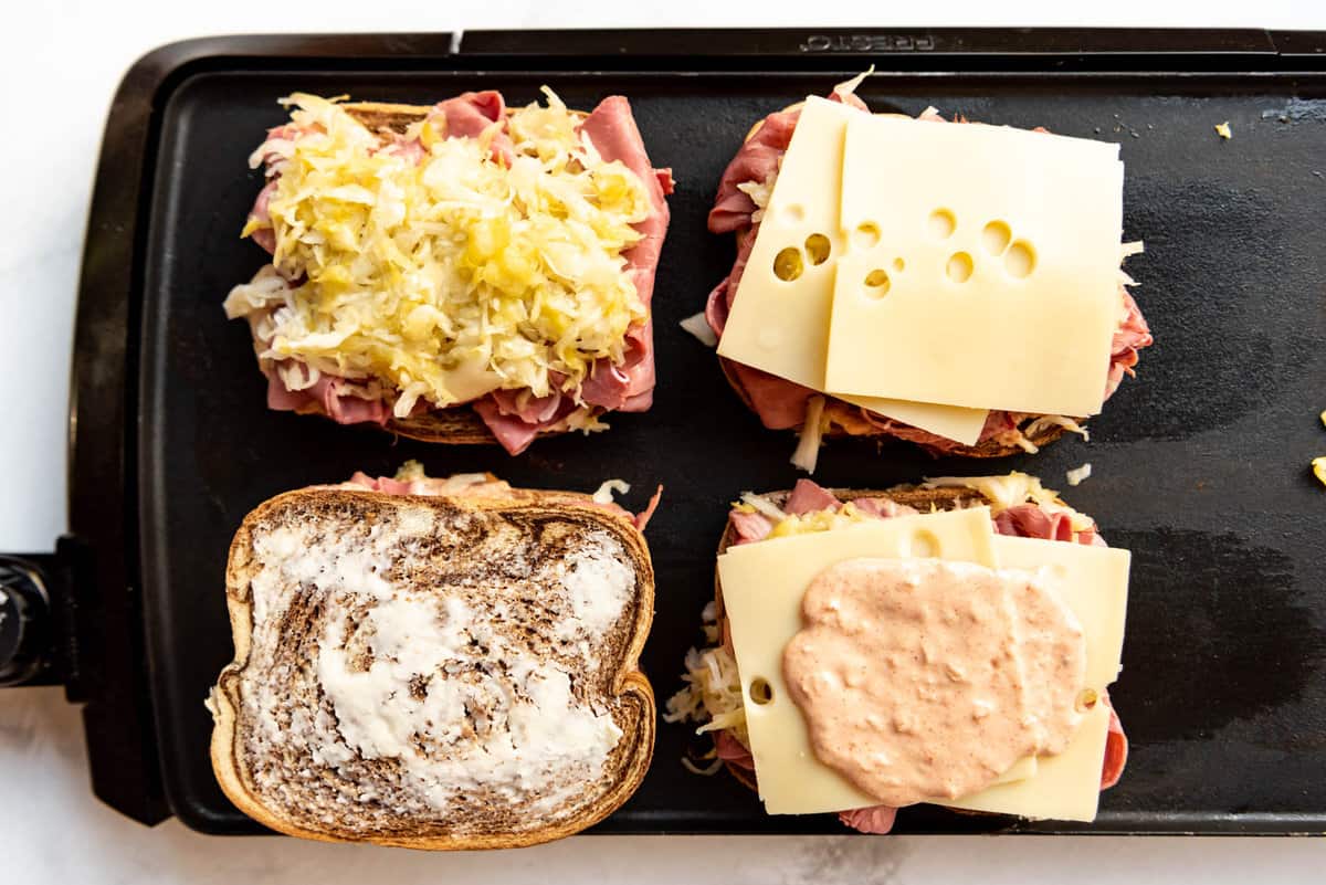 An overhead image of four reuben sandwiches being assembled on a griddle.