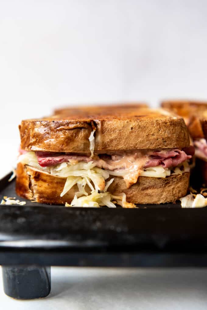A side view of reuben sandwiches being grilled on a hot griddle.