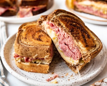 A reuben sandwich that has been sliced in half on a plate with more sandwiches behind them.
