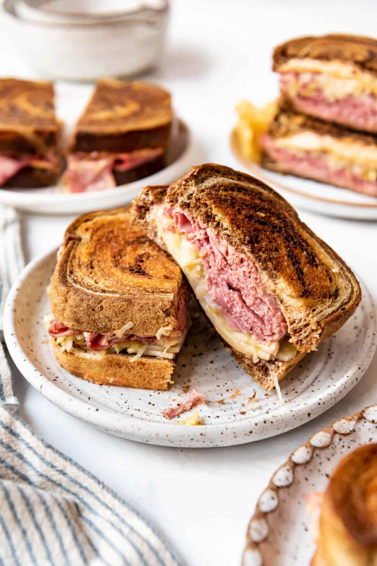 A reuben sandwich that has been sliced in half on a plate with more sandwiches behind them.