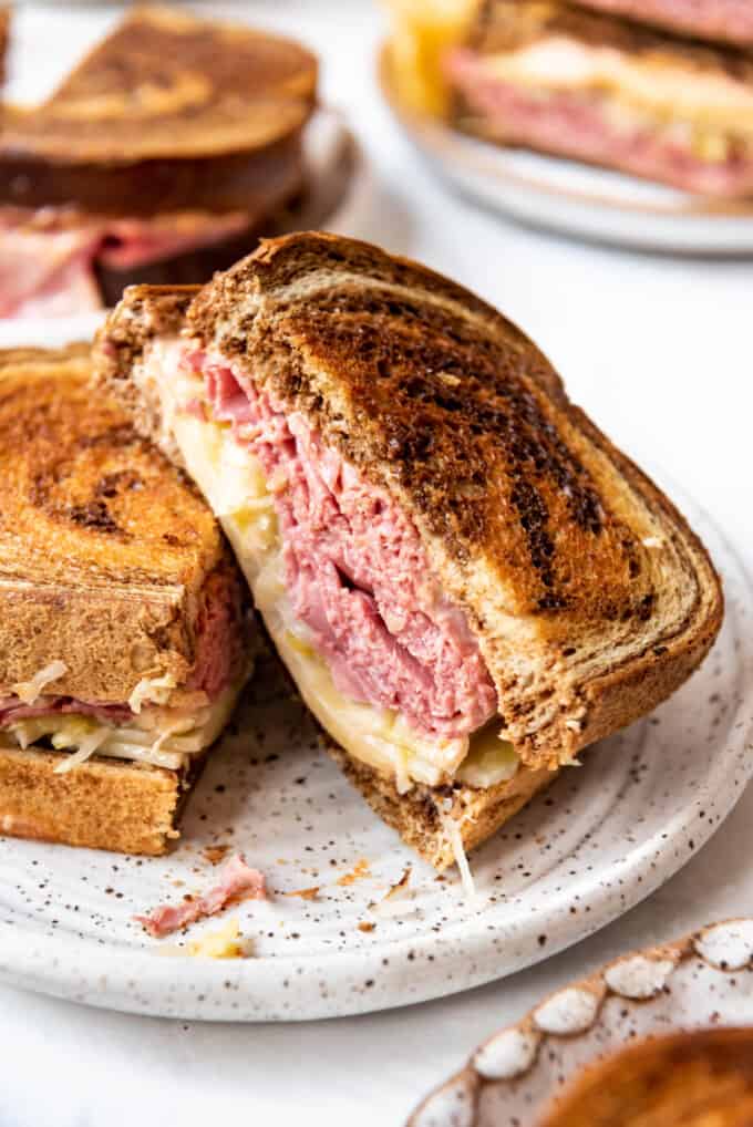 A close image of a reuben sandwich half leaning on another sandwich  on a plate.