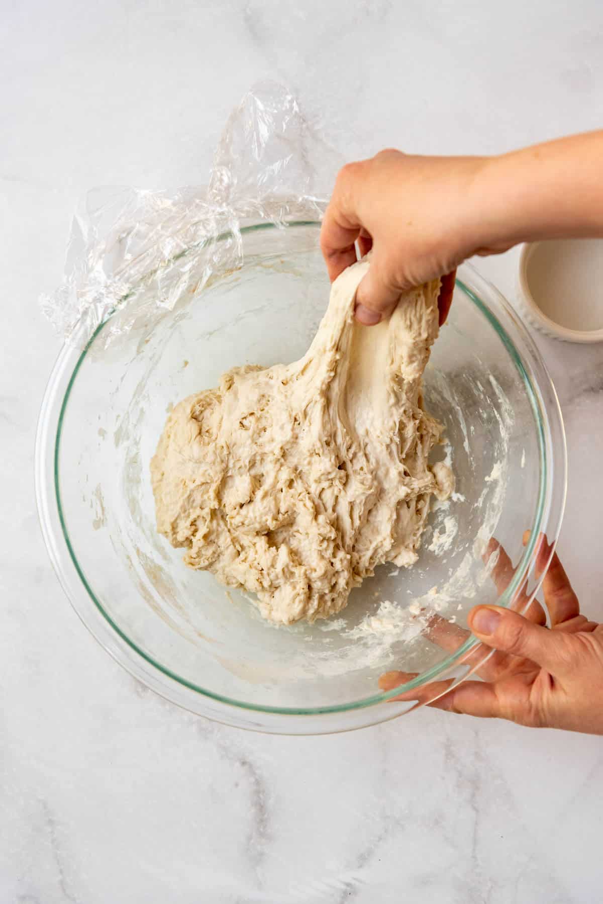 Hands stretching out sourdough bread dough for stretch and folds.