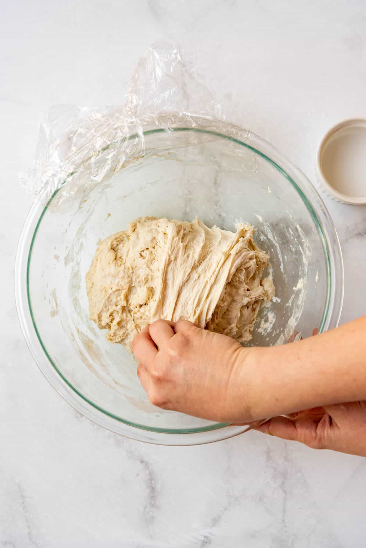 Finishing a stretch and fold on sourdough bread dough in a large glass mixing bowl.