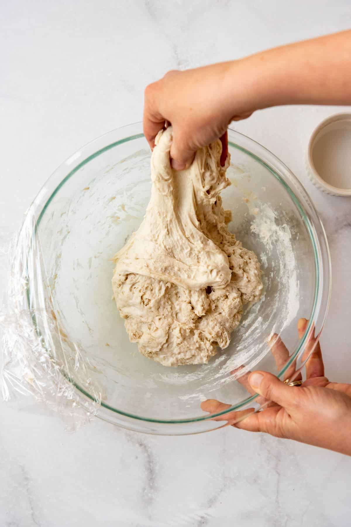 Hands stretching out sourdough bread dough in a large glass bowl for stretch and folds.