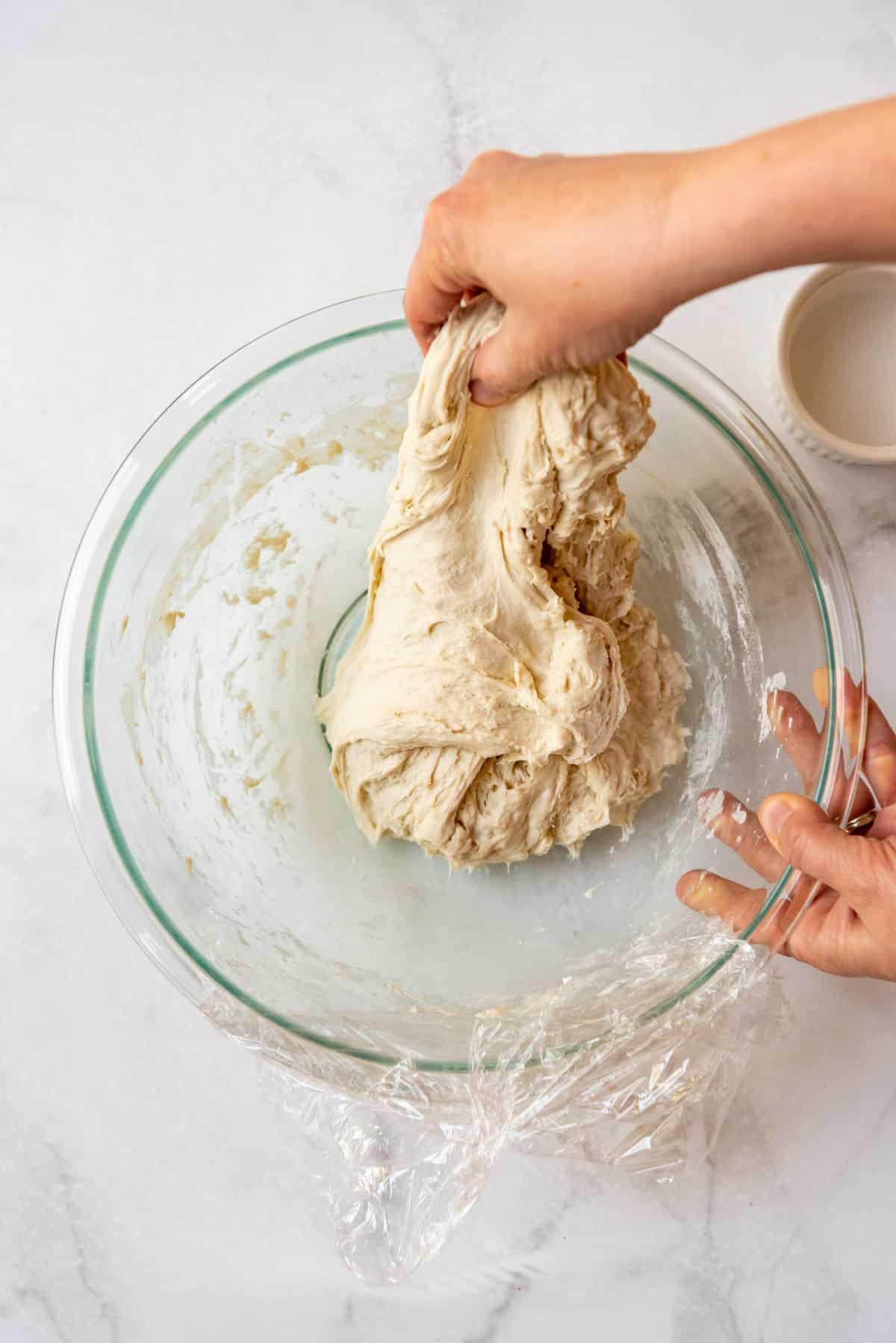 Hands stretching out sourdough bread dough in a large glass bowl for stretch and folds.