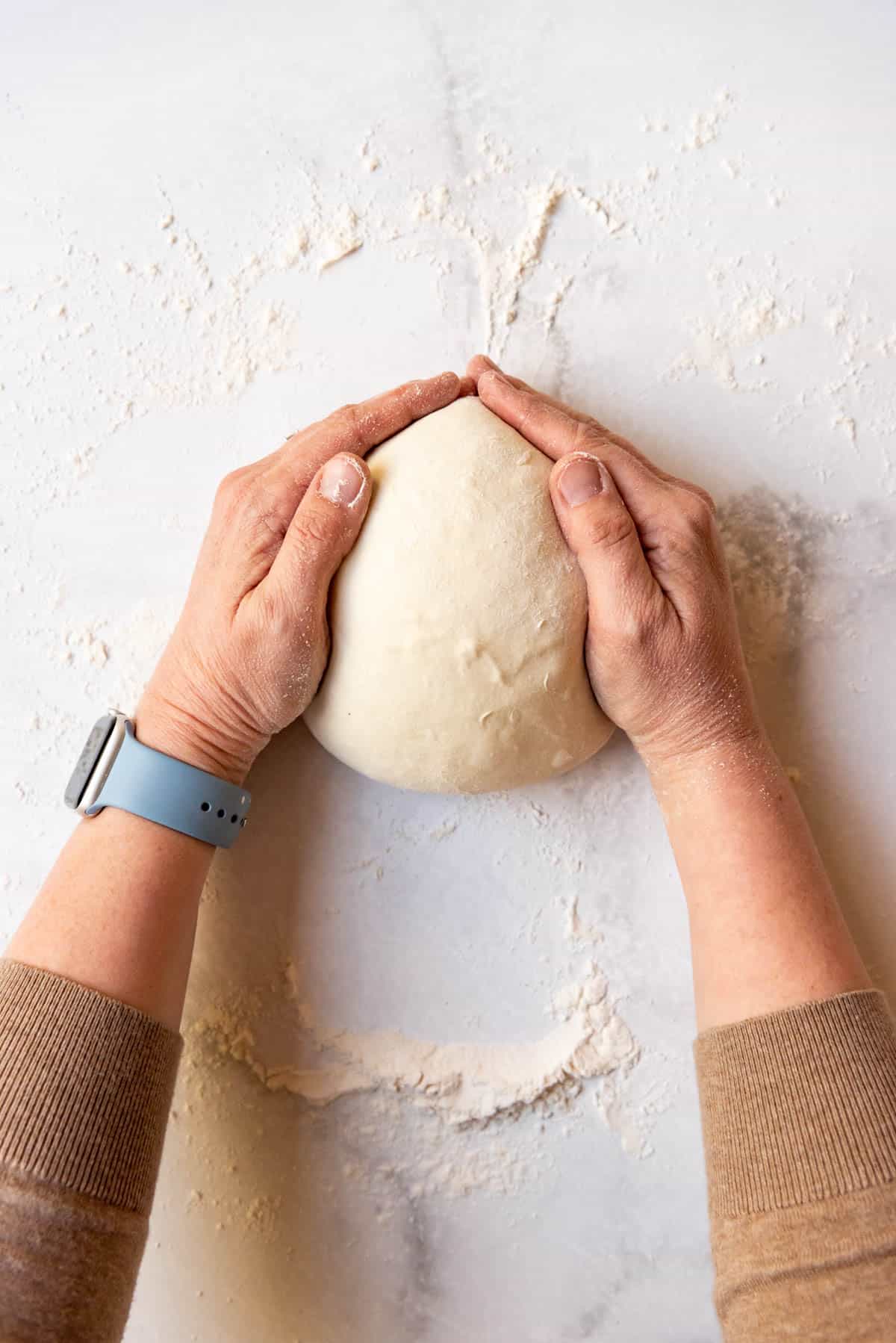 Hands pulling a ball of sourdough bread dough tight.