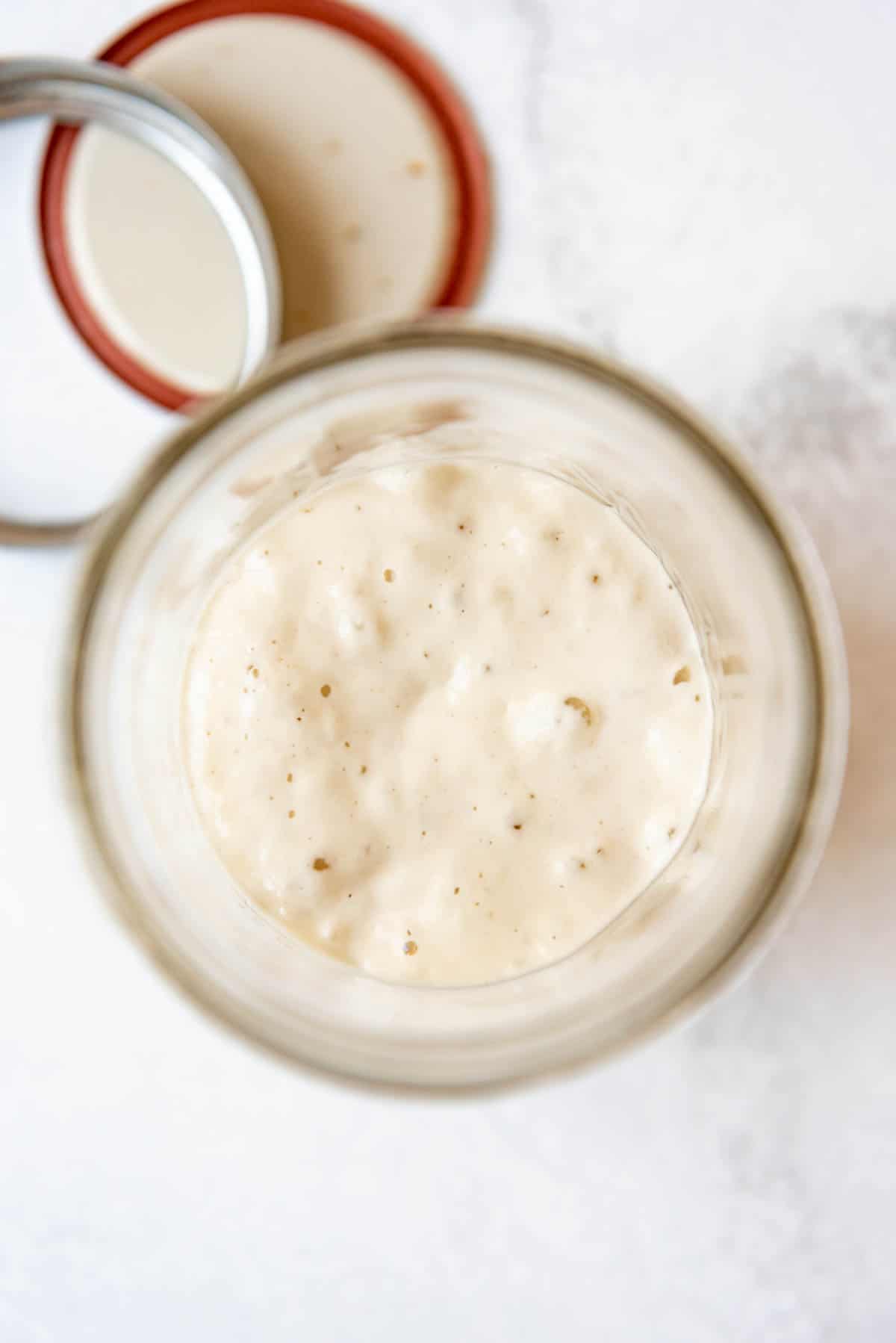 An overhead image of a glass jar of sourdough starter with bubbles on top.