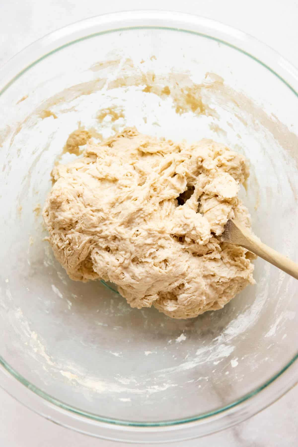 Shaggy sourdough bread dough in a bowl with a wooden spoon.