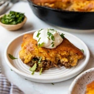 A piece of tamale pie on a plate with a dollop of sour cream on top.