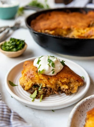 A piece of tamale pie on a plate with a dollop of sour cream on top.