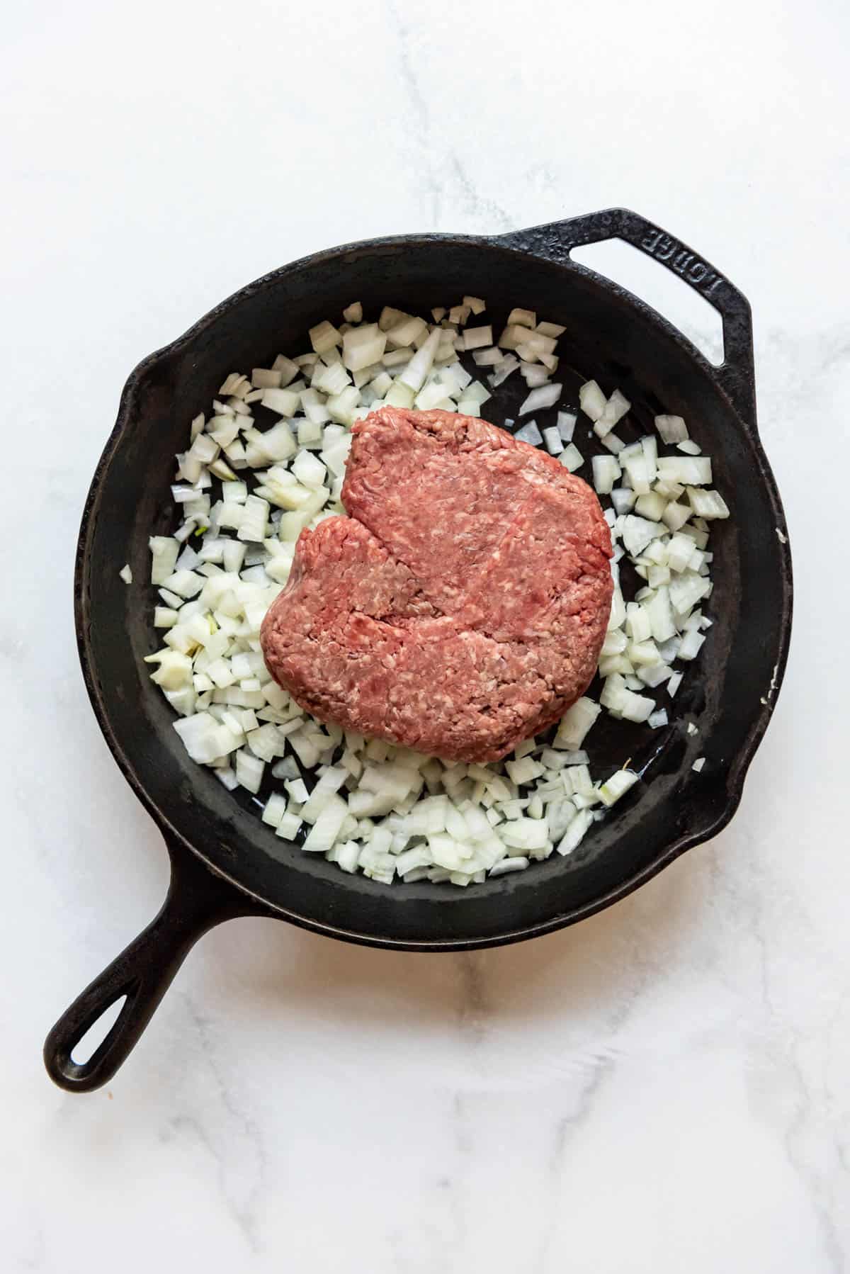 Adding ground beef to a pan of chopped onions.