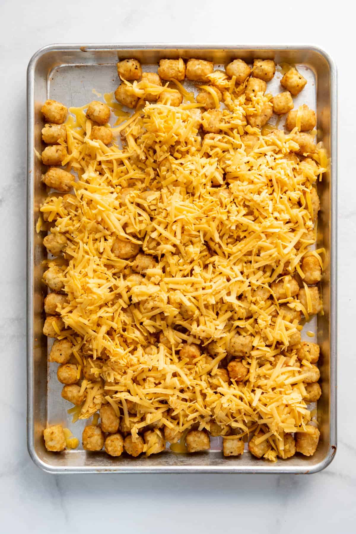 Adding a layer of shredded cheese on top of crispy tater tots.