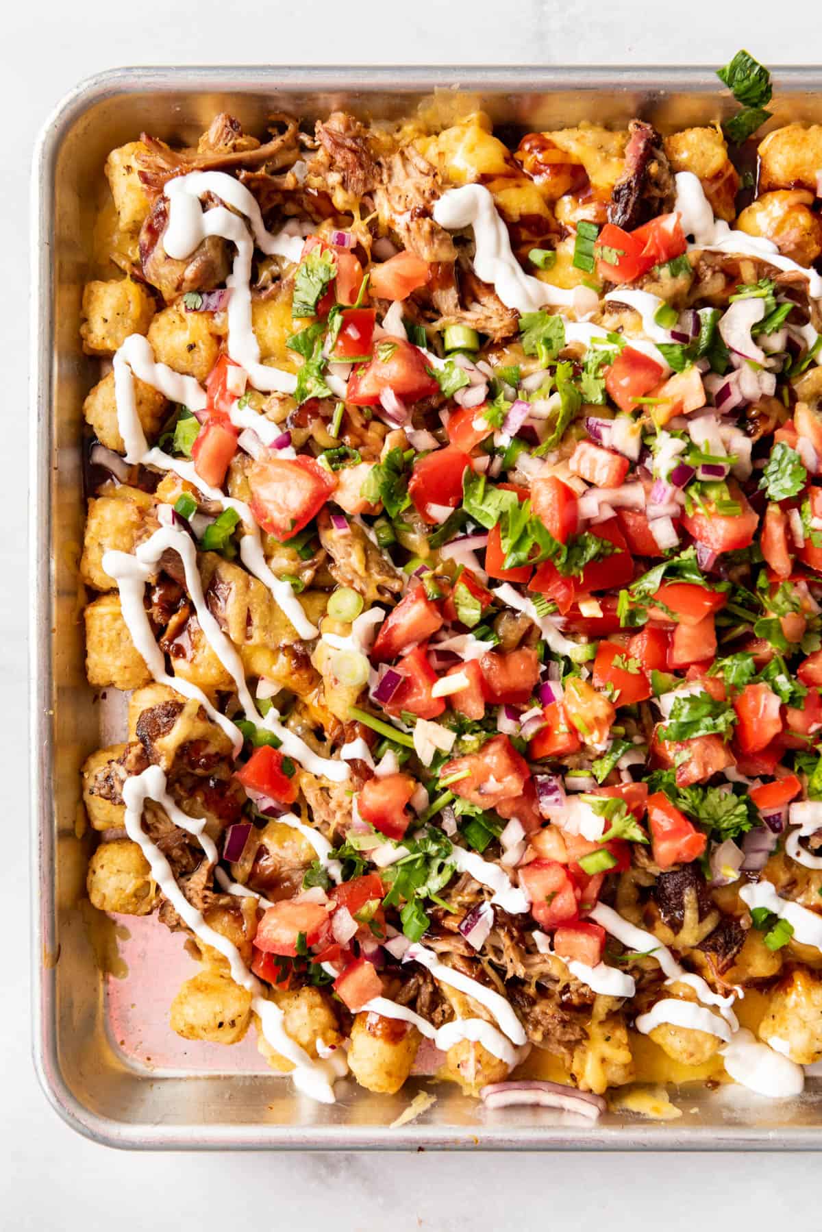 An image of loaded tater tot nachos (aka totchos) with pulled pork, pico de gallo, cheese, and sour cream.