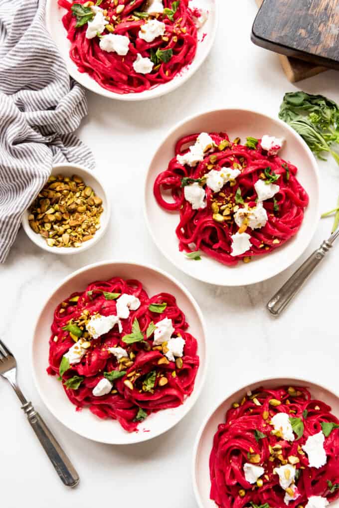 Bowls of TikTok beet pasta with goat cheese, fresh basil, and chopped pistachios.