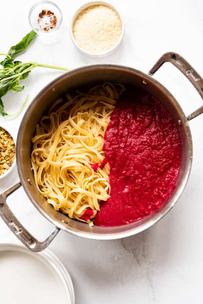 Adding beet sauce to fettucine pasta in a large pot.