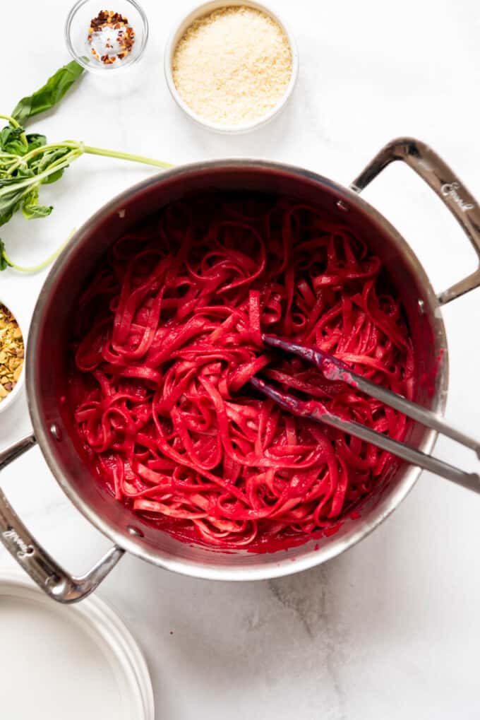 Tossing beet sauce with cooked fettucine pasta.