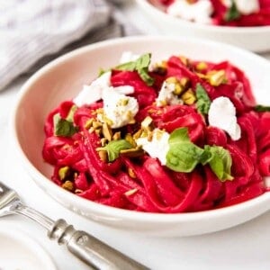 A bowl of beet pasta with goat cheese, pine nuts, and fresh basil.