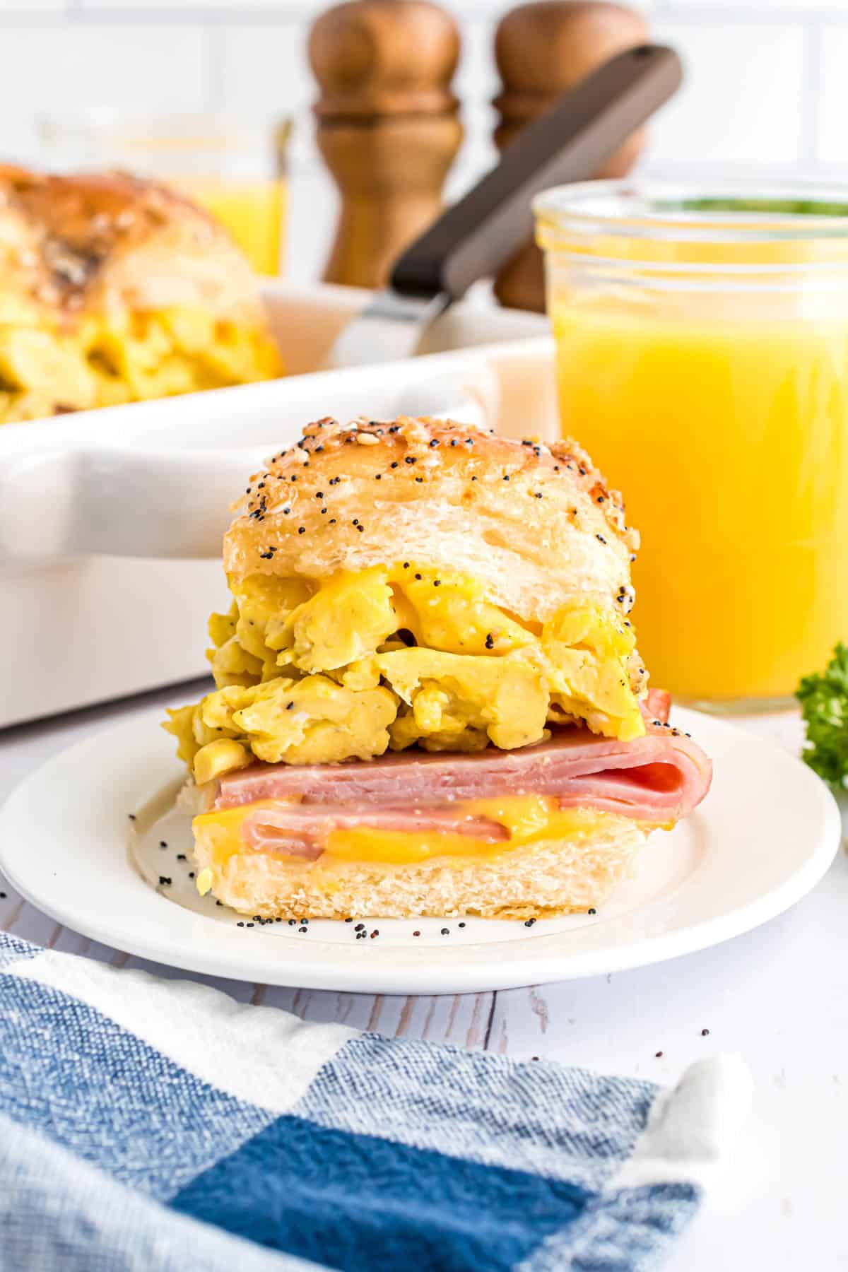 A ham, egg, and cheese breakfast slider in front of a glass of orange juice.