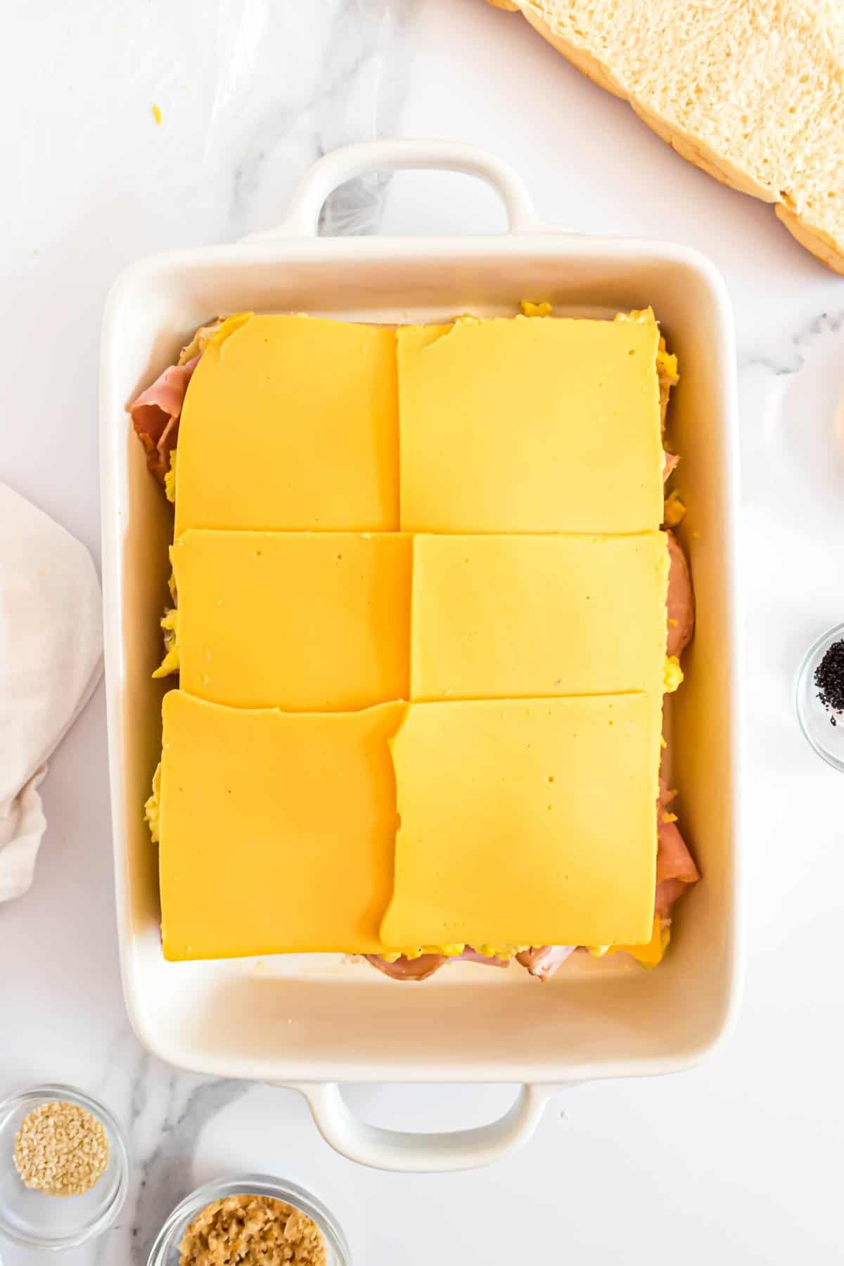 Adding more sliced cheese on top of breakfast sliders.