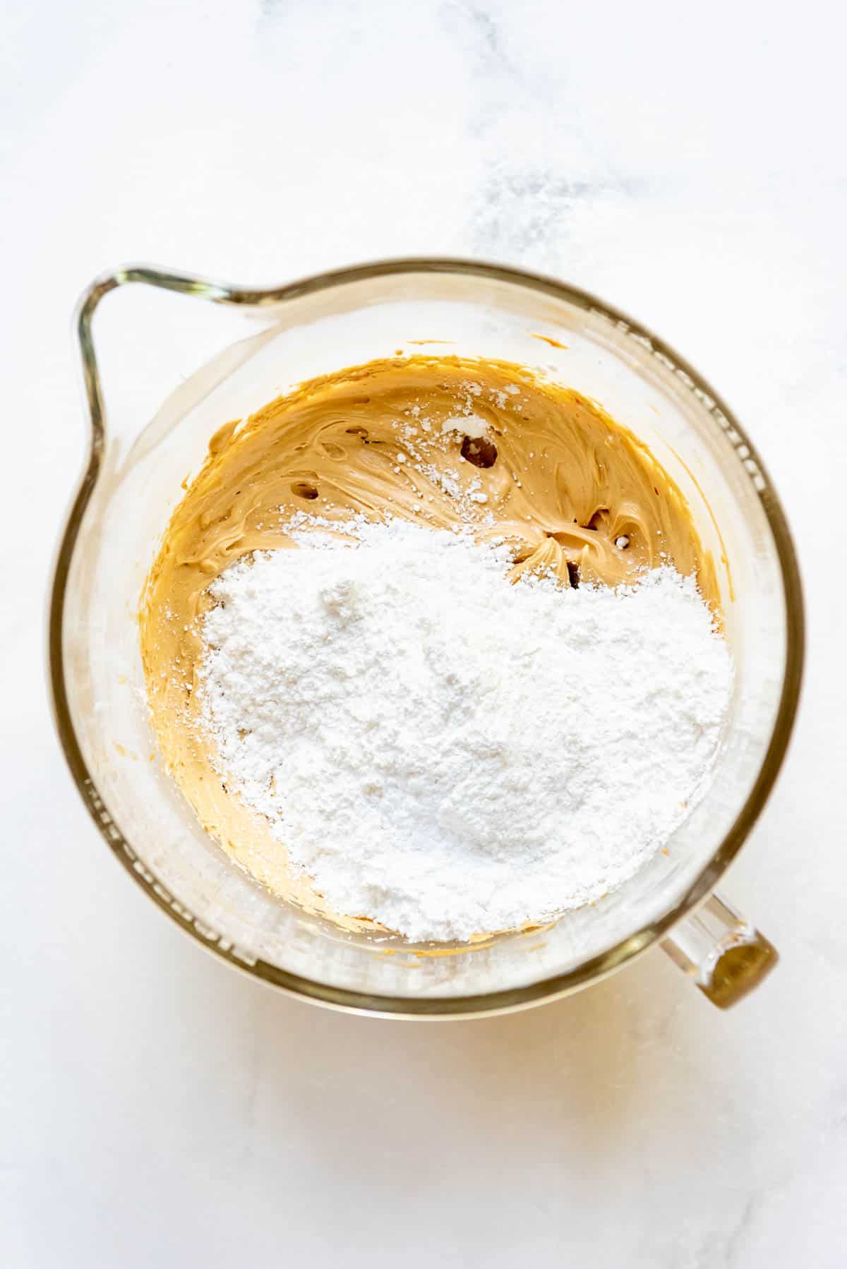 Top view of a glass mixing bowl with a peanut butter mixture in it and powdered sugar on top.