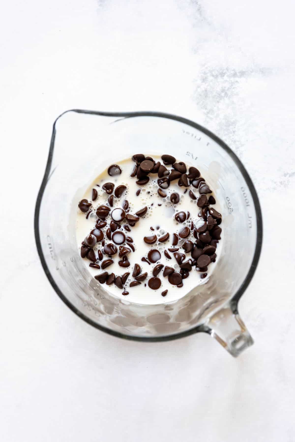 Top view of a glass mixing jug with cream and chocolate chips in it.