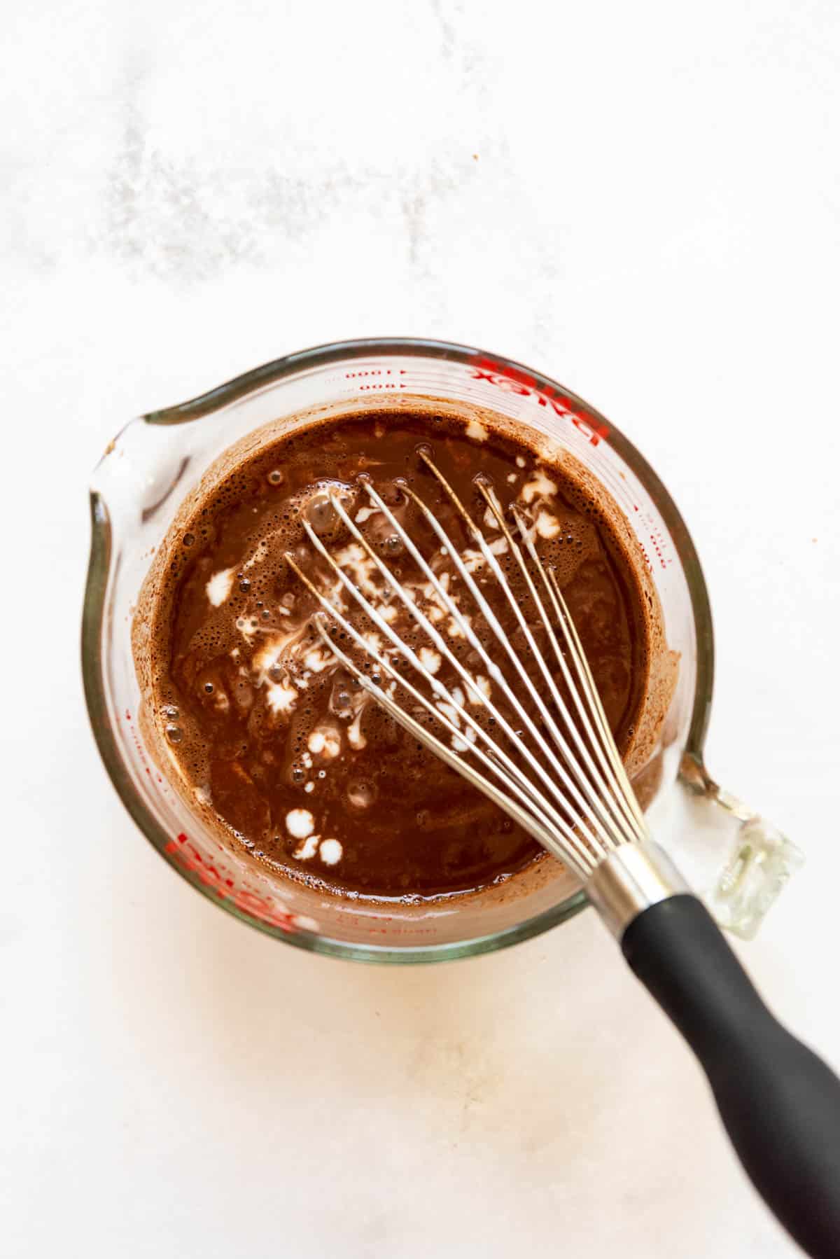 Top view of a glass measuring jug with a cocoa powder mixture, with powdered sugar and a whisk in it.