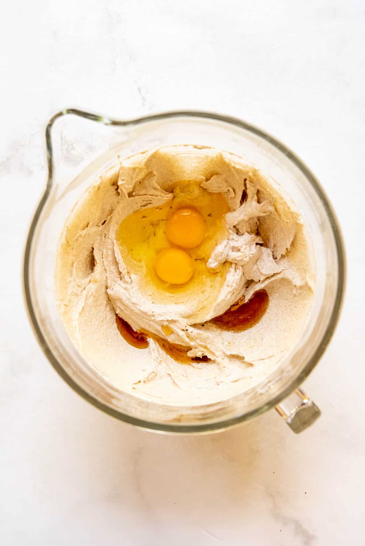 Top view of a glass mixing jug with a creamed butter and sugars mixture in the bottom and egge and vanilla extract on top.