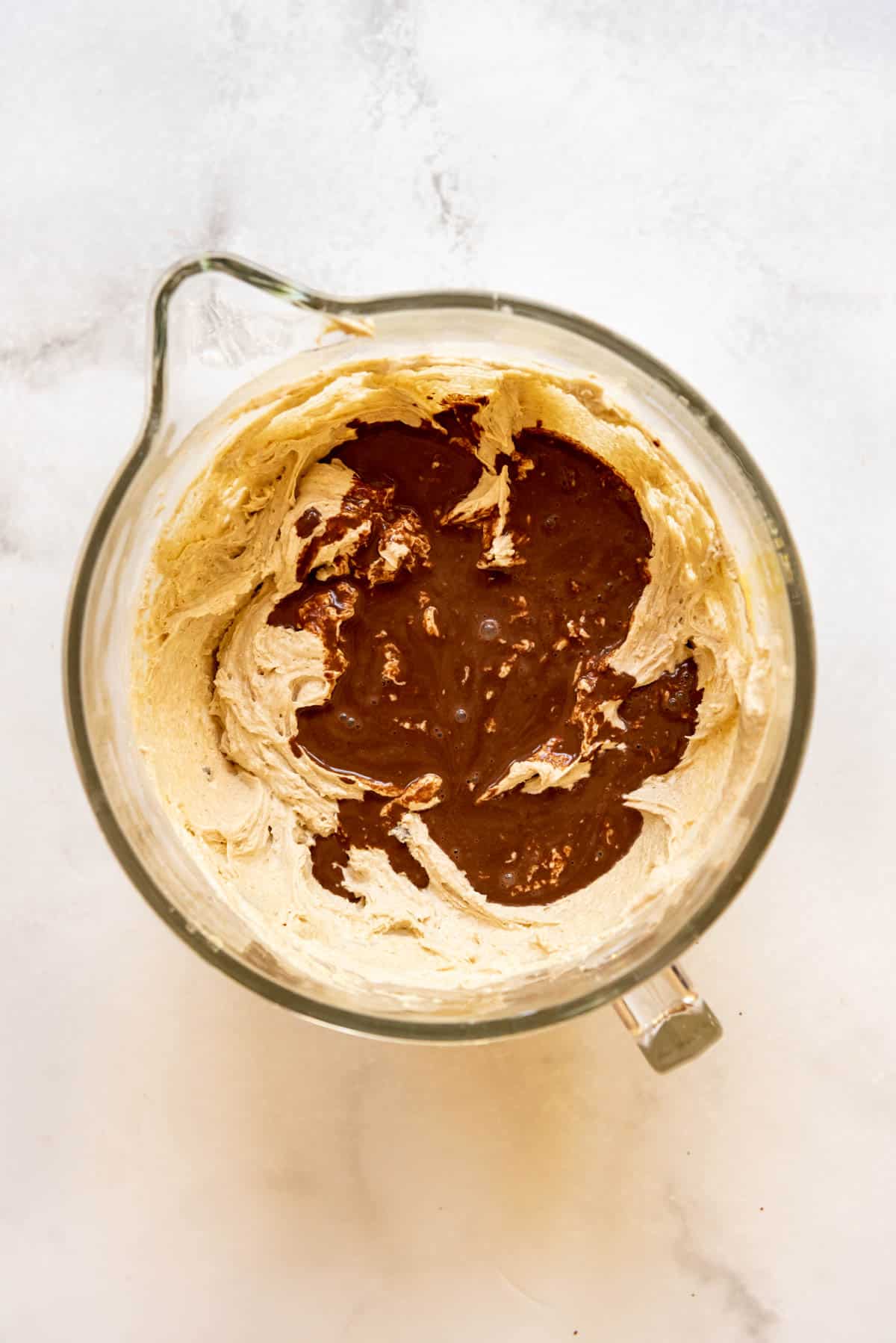 Top view of a glass mixing jug with cake mixture in it and cocoa powder on top.