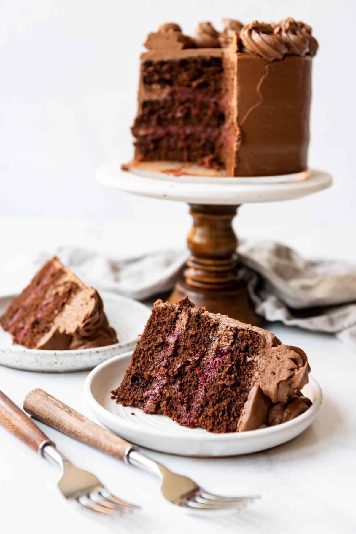 Slices of chocolate raspberry cake on plates in front of the rest of the cake on a cake stand.