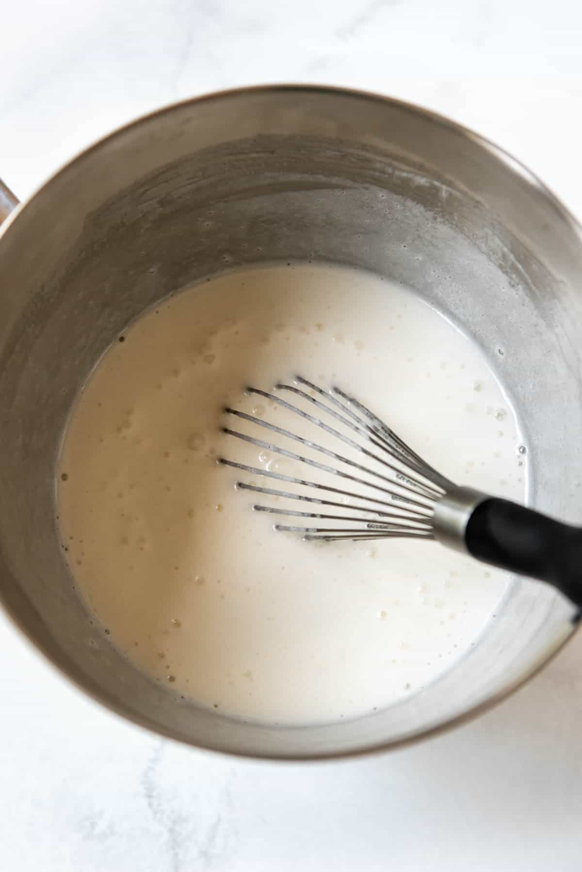 Frosting egg whites and sugar with a whisk in a mixing bowl.