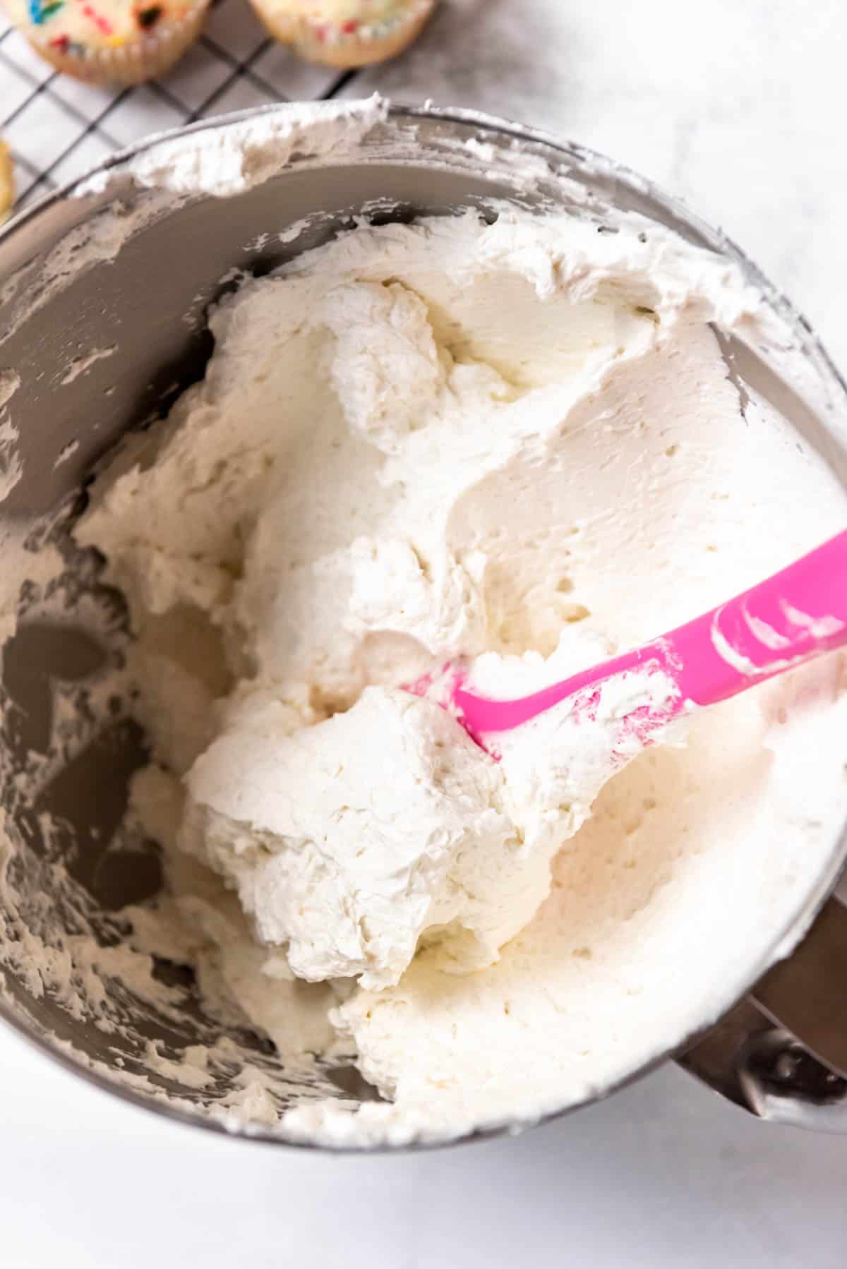 A pink spatula in a bowl full of white Swiss meringue buttercream frosting.