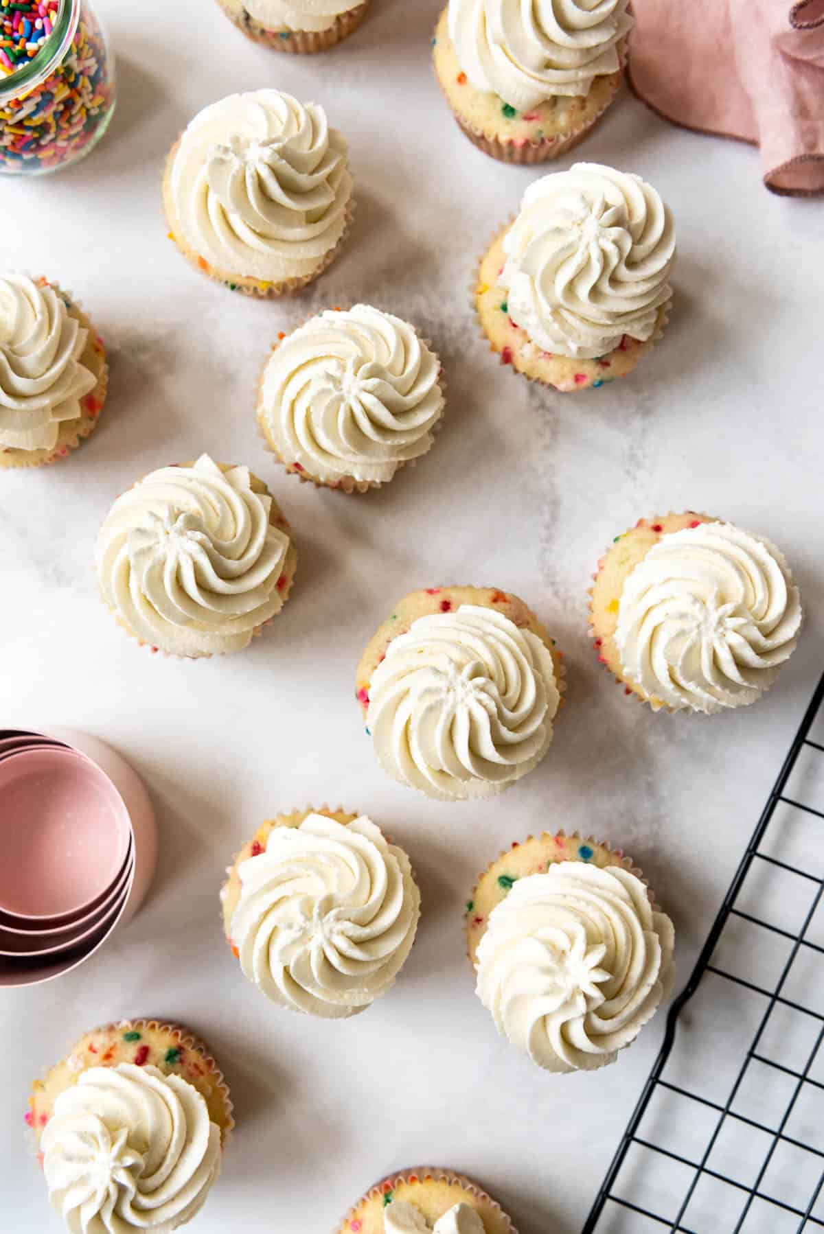 An overhead image of cupcakes decorated with swirls of white Swiss meringue buttercream frosting.