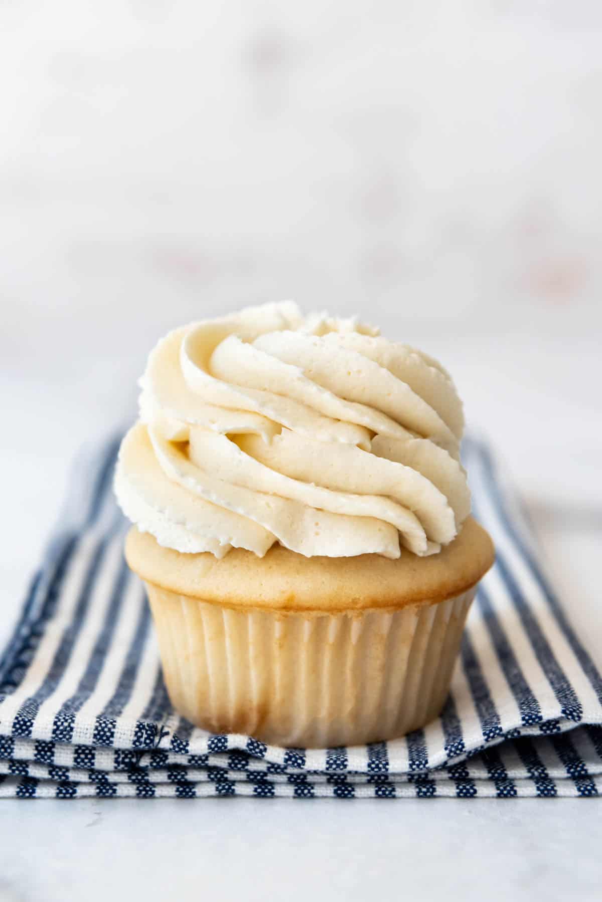 A white cupcake topped with swirls of white Swiss meringue buttercream.