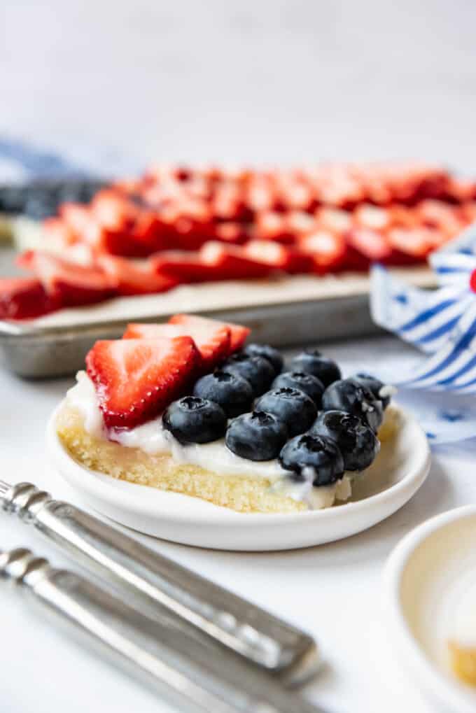 A slice of white Texas sheet cake with strawberries and blueberries on top of it.