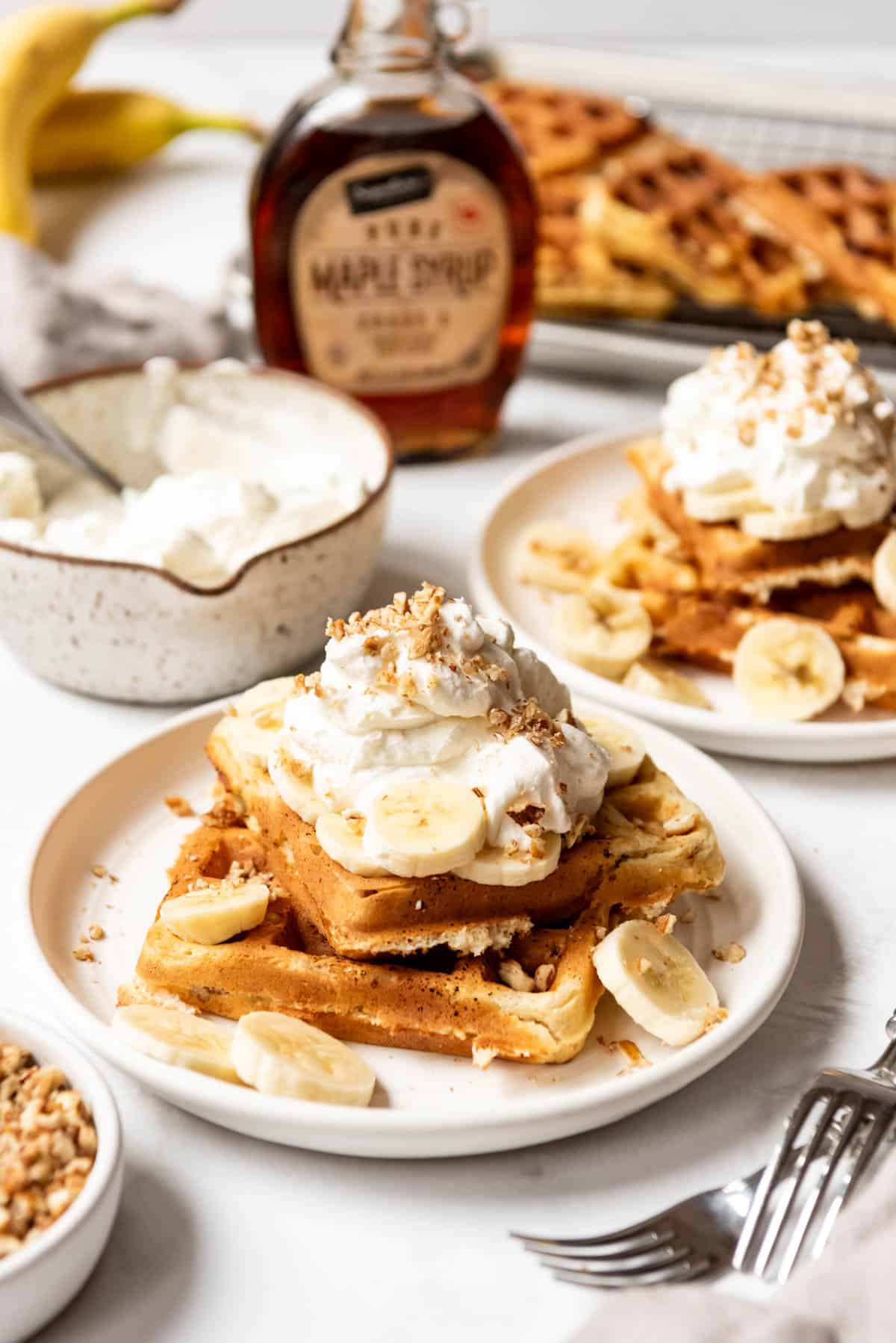 Homemade banana pecan belgian waffles on plates with freshly whipped cream.