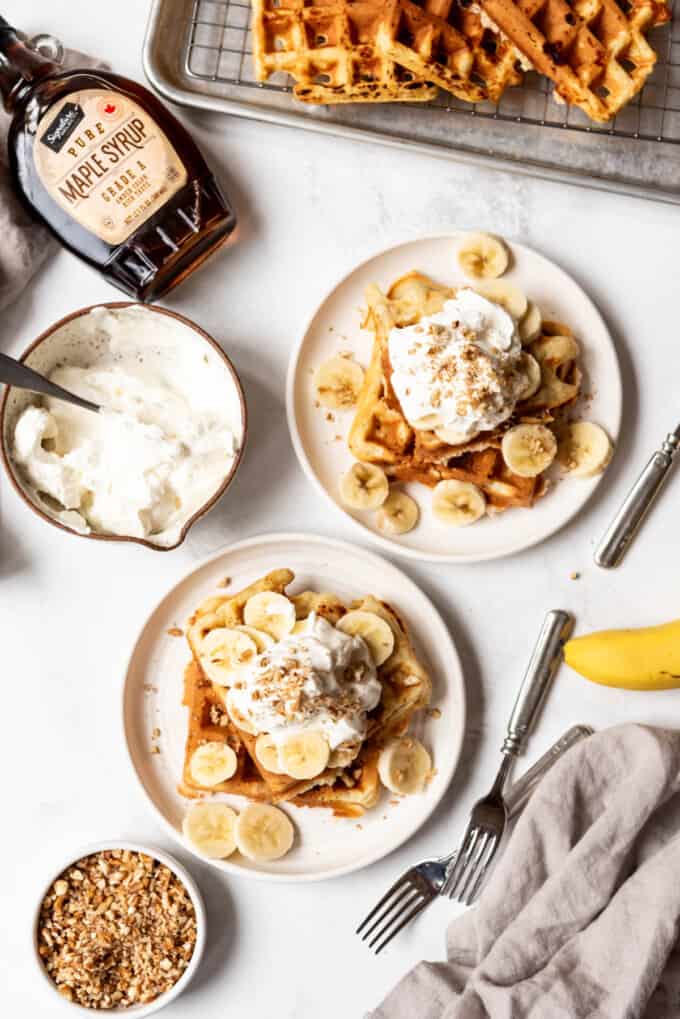An overhead image of banana pecan waffles on plates with whipped cream and fresh bananas.