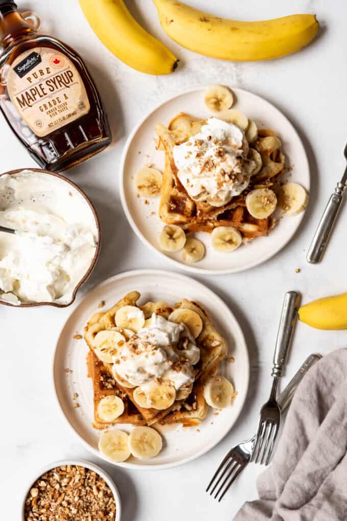 An overhead image of two plates of banana pecan waffles with bananas next to them.