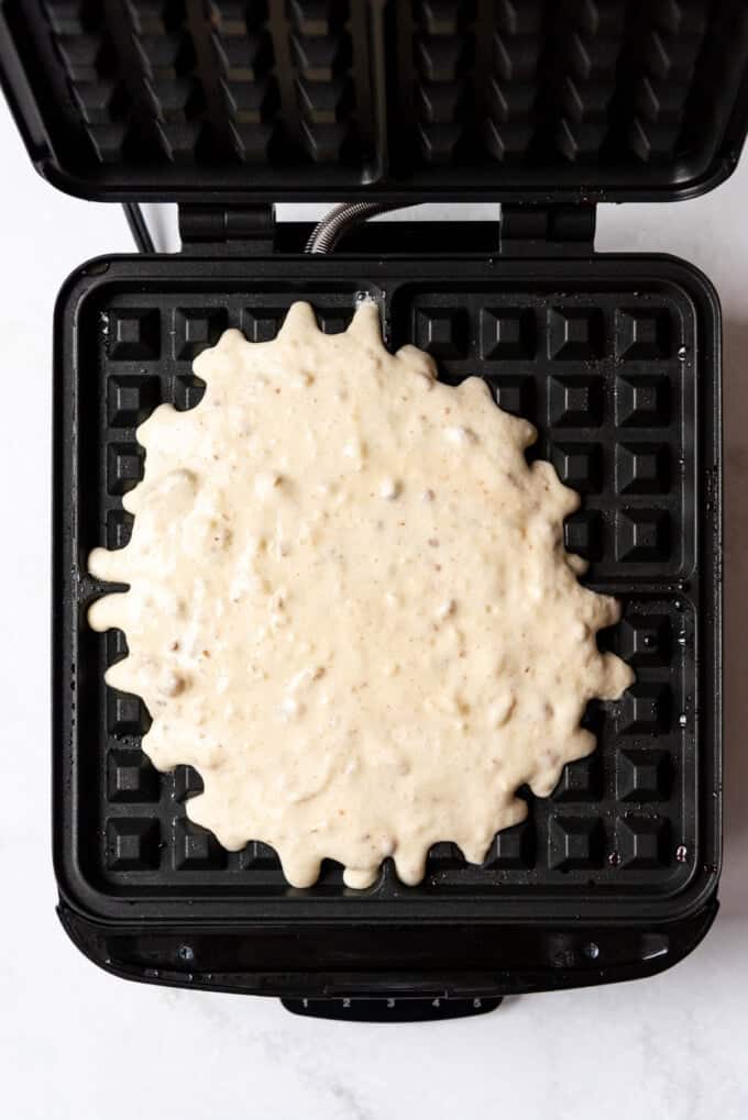 Adding pecan waffle batter to a large belgian waffle maker.