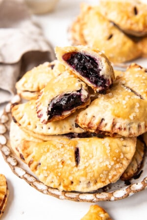 Blueberry hand pies stacked on a plate with the top one broken in half to show the filling inside.