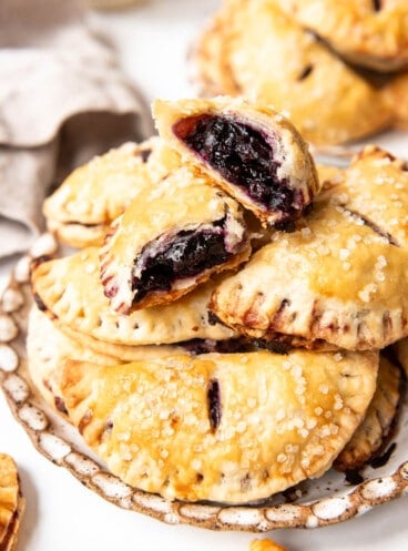 Blueberry hand pies stacked on a plate with the top one broken in half to show the filling inside.